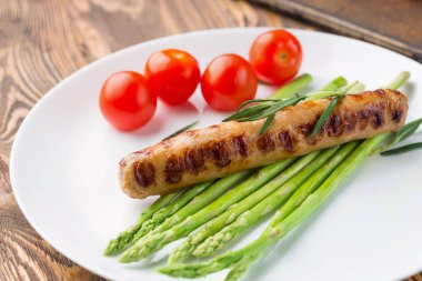 Beyaz tabakta kuşkonmaz ile kızarmış sosis, ahşap masa.