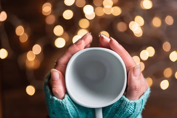 Руки жінки тримають порожню білу чашку. Різдвяні вогні . — стокове фото