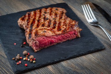 Dilimlenmiş az pişmiş biftek biftek, pirzola ve ahşap arka planda siyah taş tahtada kızartılmış.