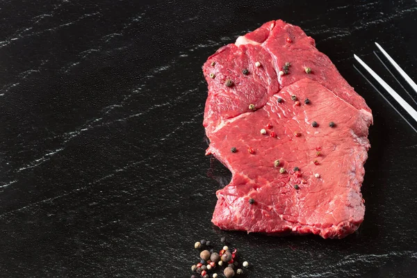 新鲜的生牛肉肉 黑板背景下有叉子和香料的新鲜红肉片 免版税图库图片