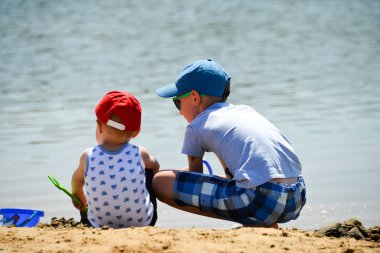kumsalda oturuyor oyuncaklarla oynayan iki küçük çocuk
