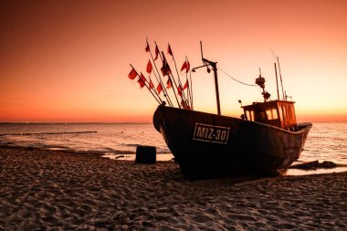 Gün batımında Baltık sahilde balıkçı teknesi