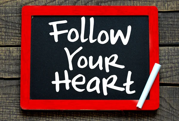 Follow your heart handwritten with white chalk on a blackboard on wood background