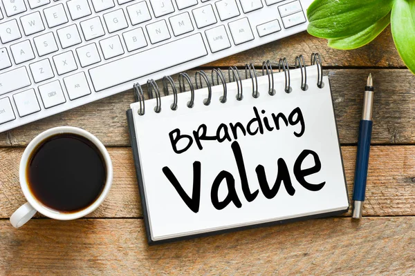 branding value handwritten on notebook with coffee cup and pen near keyboard on wooden background