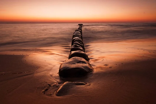 背景に劇的な日の出と砂浜を行に配置された石の景色 — ストック写真