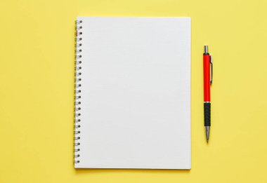 sarı arka plan üzerinde boş not defteri ve kalem ve yeşil bitki ile çalışma yeri üst görünümü 