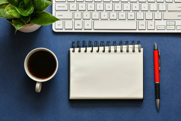 青い背景に空のメモ帳 キーボード コーヒーと緑の植物のカップと作業場所のトップビュー — ストック写真