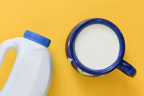 Blue cup of milk with bottle on yellow background