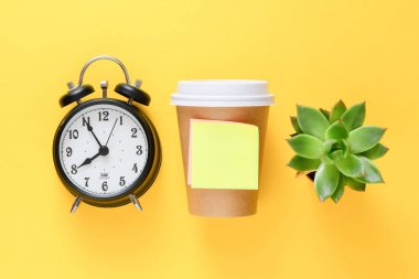 Kahve gitmek ve boş yapışkan not, çalar saat ve sarı arka plan üzerinde yeşil sulu bitki