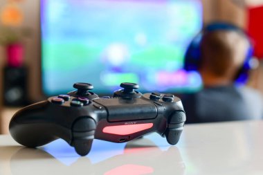 Poznan, Polonya, 23 Temmuz 2019: PlayStation 4 denetleyici. Bulanıklık TV arka plan önünde video oyun kumandası-oyun konsepti