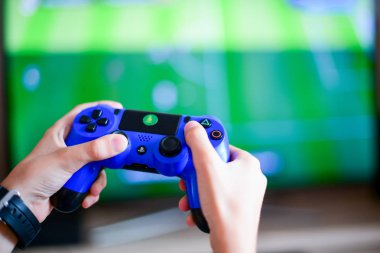 Poznan, Polonya, 23 Temmuz 2019: PlayStation 4 denetleyici. Video oyun denetleyici önünde bulanık TV arka plan-oyun kavramı. Gamepad ile oynayan kişinin kırpılmış shot