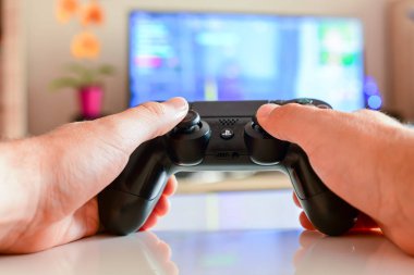 Poznan, Polonya, 23 Temmuz 2019: PlayStation 4 denetleyici. Video oyun denetleyici önünde bulanık TV arka plan-oyun kavramı. Gamepad ile oynayan kişinin kırpılmış shot