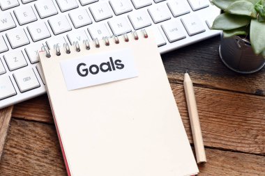 Hedefler. Bir ofis defteri ve ahşap masa üzerine beyaz bir kağıt üzerine yazılmış GOALS kelimesi.