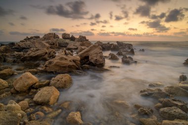 Turkuvaz suları, kumlu bir plaj, kayalık kıyı şeridi ve açık mavi gökyüzü içeren nefes kesici Kıbrıs Akdeniz manzarası. Yaz tatilleri, turizm ve doğa aşıkları için mükemmel bir tatil yeri..