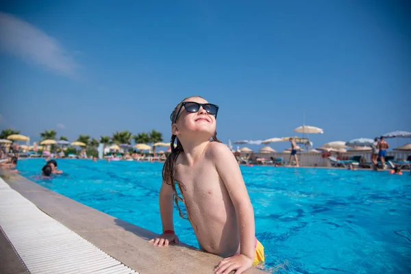 Güneş gözlüklü bir beyaz kız mavi bir havuzdan tarar