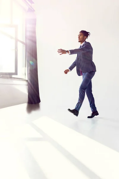 Businessman in a blue suit walks like a zombie to the light from a window. White background