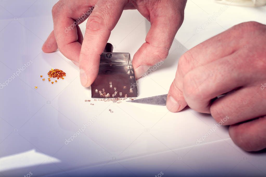 The hands of a man hold a scoop and sort diamonds