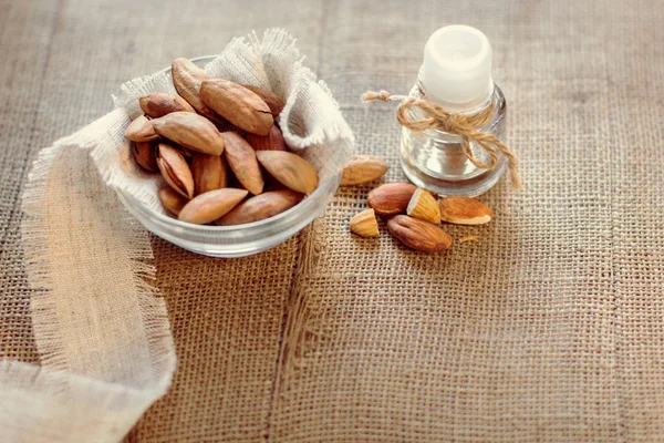 bottle with an almond\'s oil and almonds in a glass saucer on a sackcloth