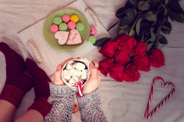 レディース足 靴下の中と赤いバラ セーター ストライプ ロリポップの中心部とベッドでの朝食とコーヒーのカップ 盆にマシュマロ マカロン ジンジャーブレッド クッキー 聖バレンタインの日のためのある静物 — ストック写真