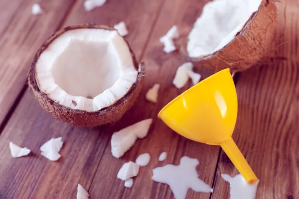 two half of coconut with yellow funnel and spilled milk on a wooden background