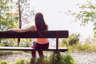 bir kız ormanda bir bankta oturur, kameraya sırtını