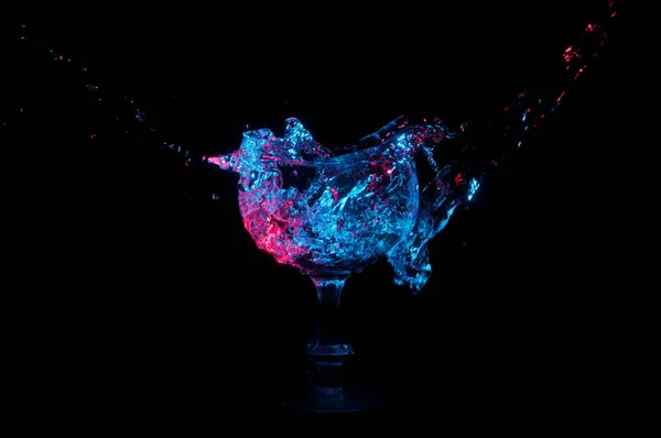 蓝色和红色的水溅入一个玻璃杯在黑色背景 — 图库照片