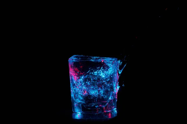 Скло, що переповнюється синьою освітленою водою на чорному тлі — стокове фото