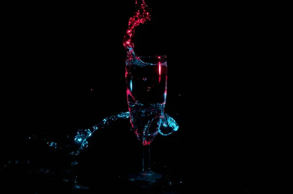 Red and blue liquid swirling around and out of a champagne glass on a black background — Stock Photo, Image