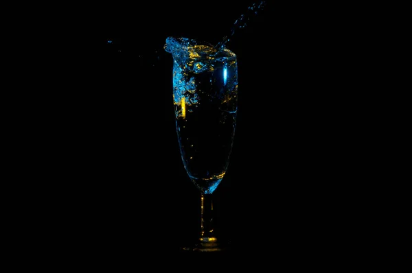 Liquido blu con riflessi gialli spruzzi da un bicchiere di vino isolato su uno sfondo nero — Foto Stock