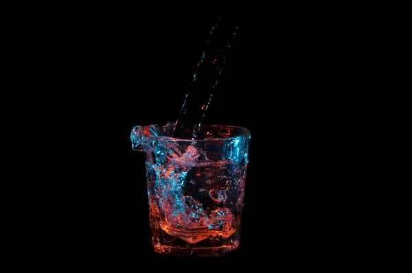 Verter en un vaso de rocas y salpicar bajo luces azules y anaranjadas aisladas sobre un fondo negro — Foto de Stock