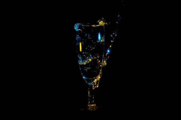Beautiful yellow and blue bubbles in a fancy glass being filled with a beverage isolated on a black background — Stock Photo, Image