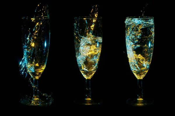 Tre bicchieri sotto le luci blu e oro vengono riempiti progressivamente con liquido trasparente su uno sfondo nero Foto Stock Royalty Free