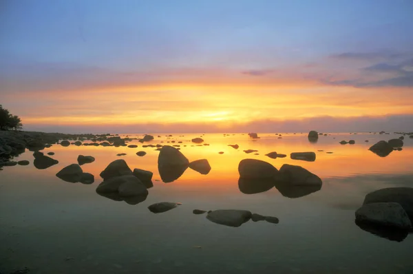 Pôr-do-sol quente em um céu azul sobre uma praia rochosa com água parada Fotos De Bancos De Imagens