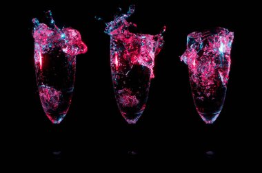 Üst üste üç özdeş şampanya lale gözlük siyah bir zemin üzerine sıçramasına berrak sıvı içinde parlak ışıklı kırmızı ışık mavi vurgulamaktadır