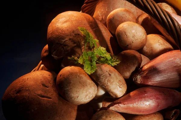 Primo piano di funghi, scalogno e prezzemolo sotto un'illuminazione calda in un cesto di vimini marrone Immagine Stock