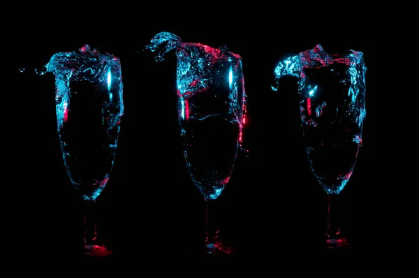 青と黒の背景に つのシャンパン チューリップ グラスの行に赤で燃えるような透明な液体のカラフルな水しぶき — ストック写真