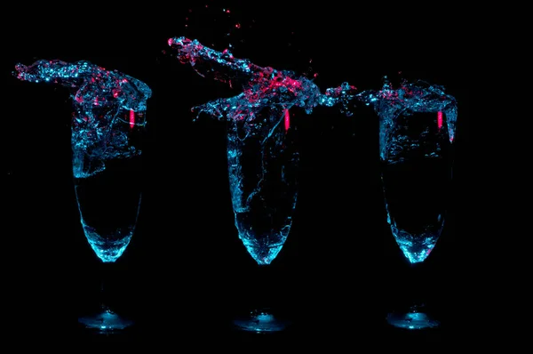 3 の派手なメガネを黒の背景に赤のアクセントを持つ透明な液体と青いライトの下で大きなスプラッシュをそれぞれの完全 — ストック写真