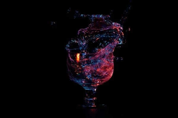 Water in vibrant colors splashing out of a glass