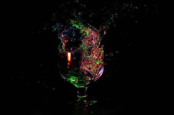 Éclaboussure colorée d'alcool dans un verre sur fond noir — Photo