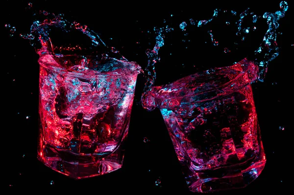 Rocas vasos tostadas y salpicaduras brillante líquido aislado sobre un fondo negro — Foto de Stock