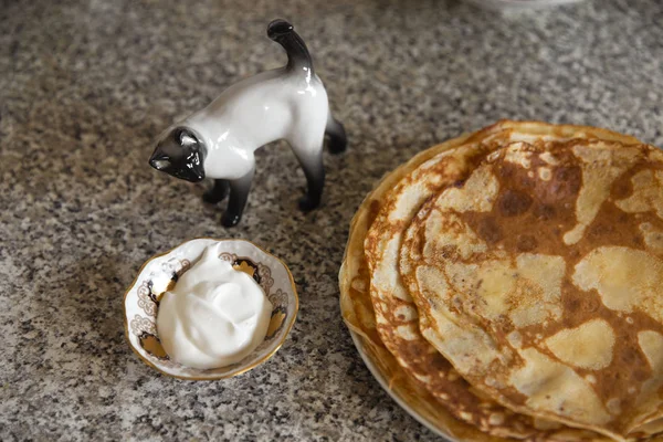 Lívance se zakysanou smetanou na kithcen stůl a porcelánové soška kočka — Stock fotografie