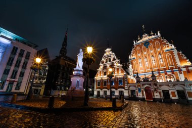 Riga, Letonya - 17 Mart 2019: Profesyonel uzun pozlama Blackheads House, Roland ve St. Peters kilise heykeli karşı karşıya yağmurlu bir gecede vurdu