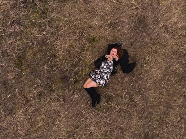 Aerial drone top view of a girl lying in a field relaxing and dancing. Wearing a dress with stockings