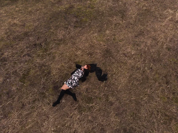 Aerial drone top view of a girl lying in a field relaxing and dancing. Wearing a dress with stockings