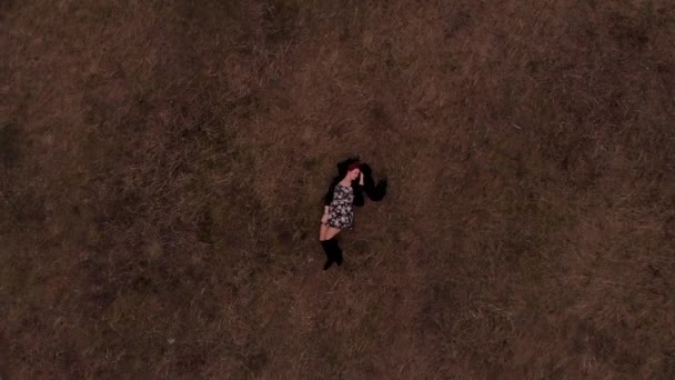 OVERHEAD DRONE знімок підліткової моделі в модному платті, лежачи на зеленій траві роблячи повільні ходи танці на землі. Модна портретна стрілянина — стокове відео