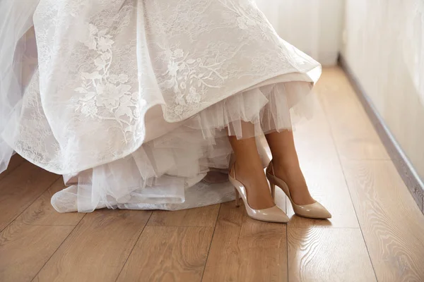 Bruden att sätta på bröllop skor hemma där shes redo - Iklädd vit klänning i ett ljust rum med trägolv — Stockfoto