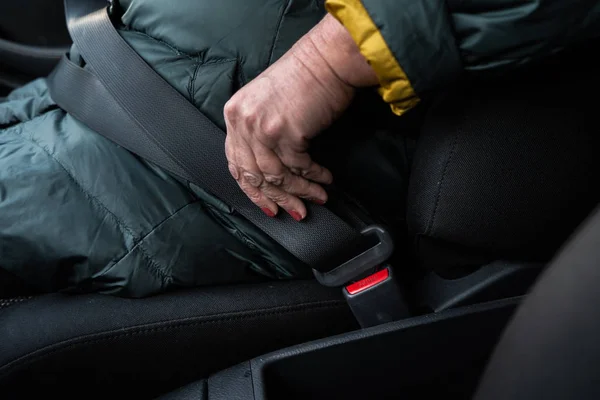 Mulher sênior mais velha prende um cinto de segurança em um carro usando casaco verde e amarelo — Fotografia de Stock