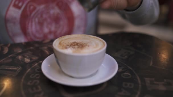 Man pours cinnamon in a cup of coffee - Closeup shot of cappuccino in a cafe — Stock Video