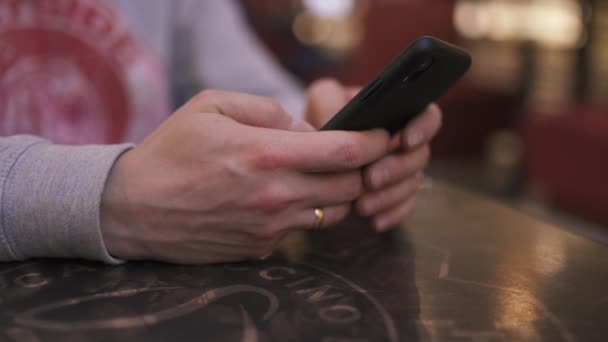 Um jovem empresário sentado em uma mesa em um café usando iphone e mensagens de texto digitando uma mensagem - Pessoas de sucesso, rotina diária — Vídeo de Stock