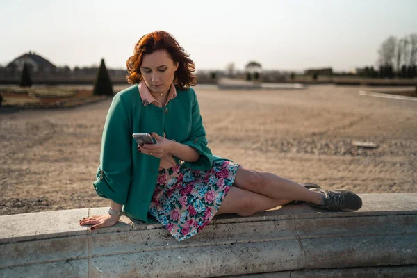 Mladá žena používá telefon v palácové parku sedící na fontáně — Stock fotografie